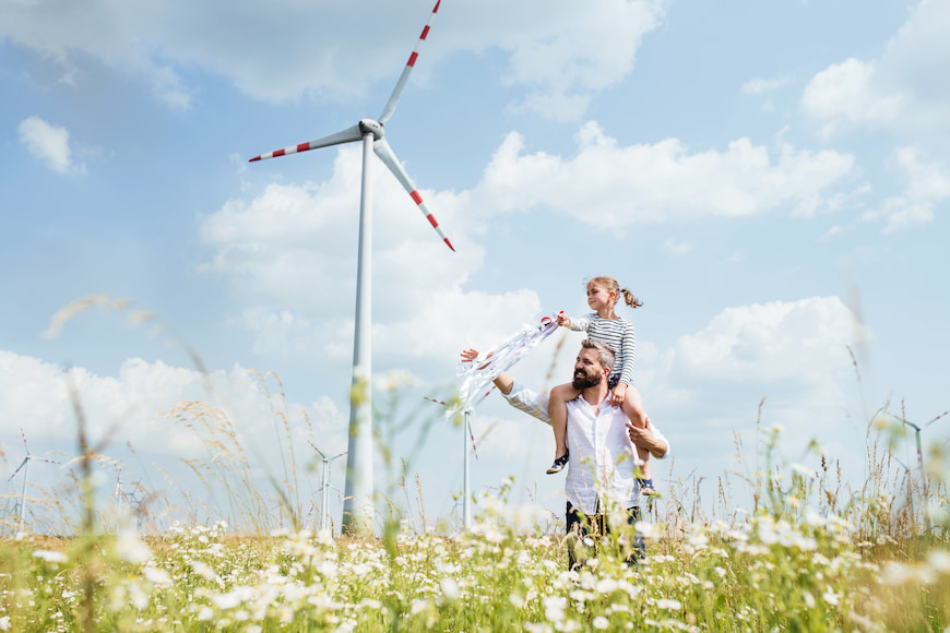 Father and daughter walking through a field with a wind turbine in the background