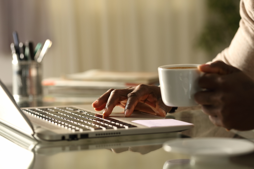 Man using computer while holding a cup of coffee.