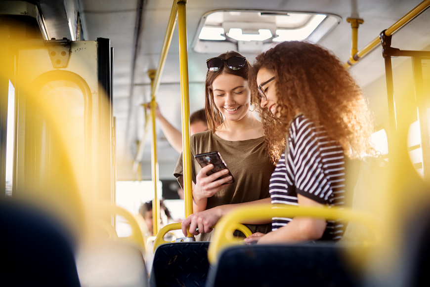 Girl on a bus showing her friends something on her cell phone