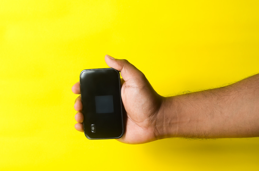 Man's hand holding a MiFi router in front of a yellow background