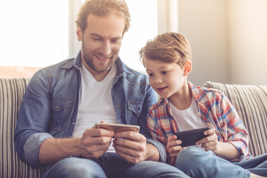 Father and Son both playing on smart phones together while sitting on the couch.