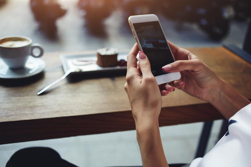 Enjoying the best mobile and phone deal - image of hand using cellphone with laptop in the background