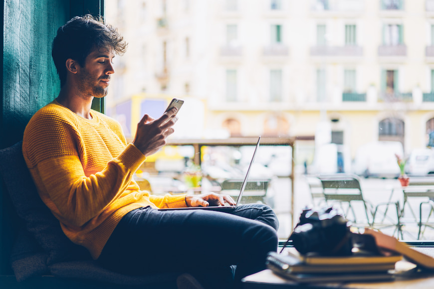 Man on his phone while also using his laptop at a café.